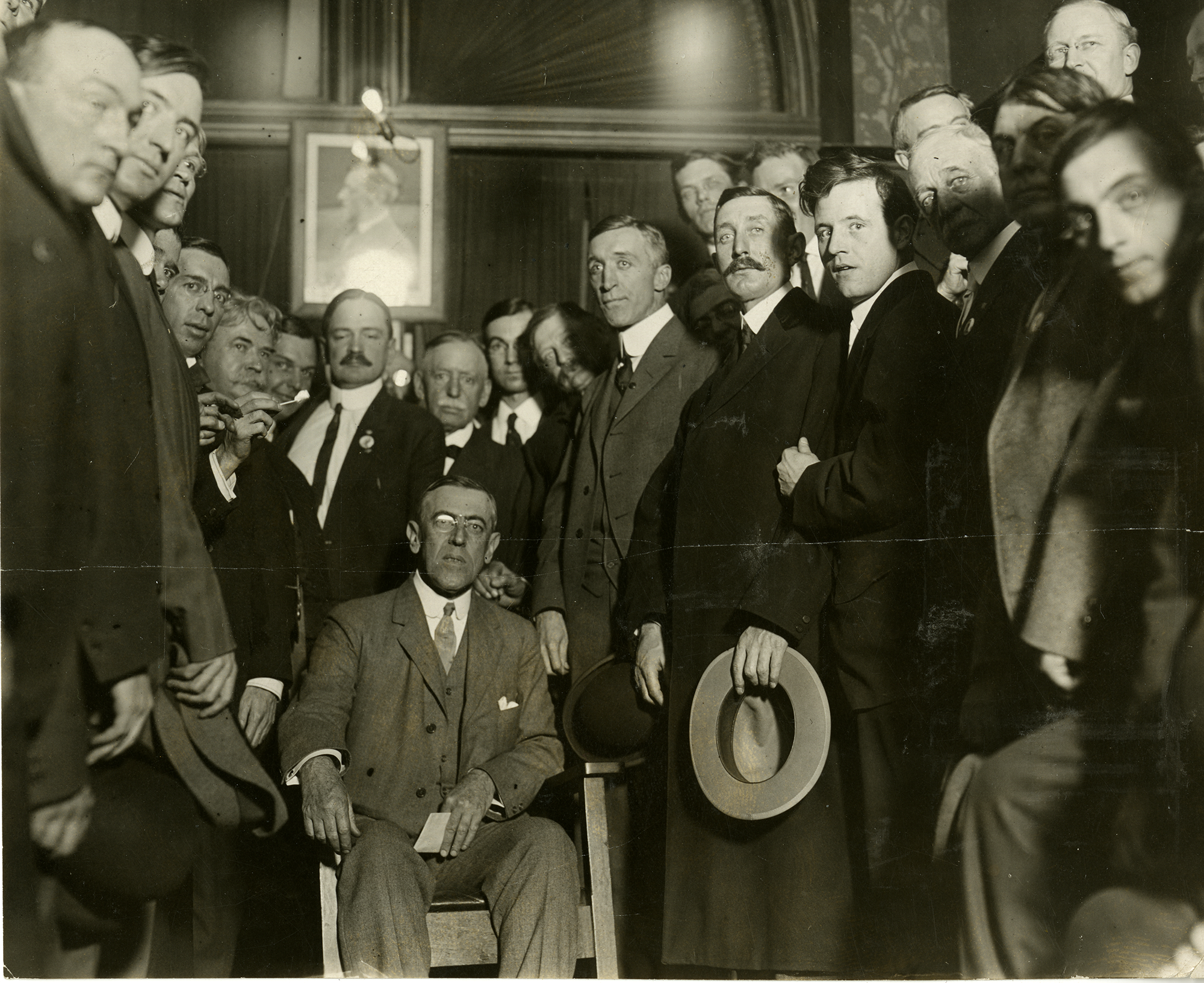 Woodrow Wilson sitting in a chair, surrounded by men in suits (members of the Denver Press Club).