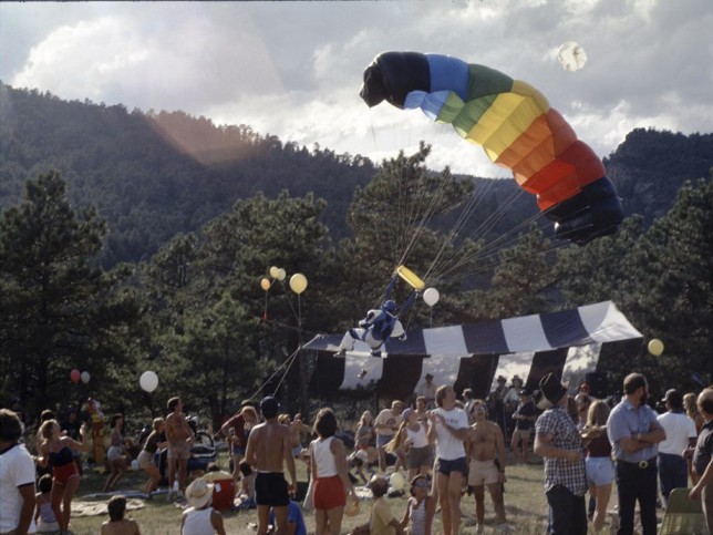 A festival in the woods with a parachutist and many partygoers.