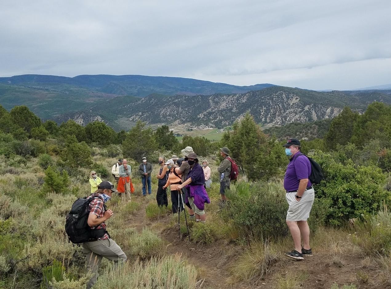 A group of hikers on the History Hike, enjoying the afternoon among shrubbery and with mountains in the distance.