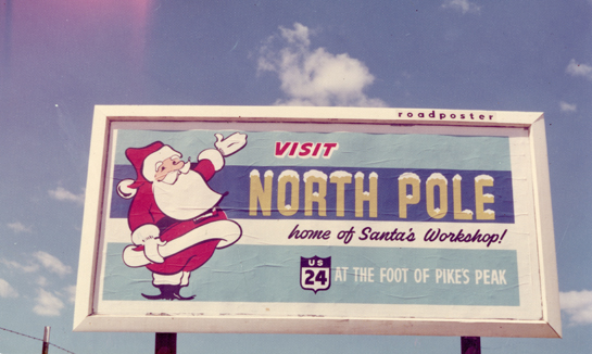 A billboard reading "Visit the North Pole, home of Santa's Workshop! US 24, at the foot of Pike's Peak."
