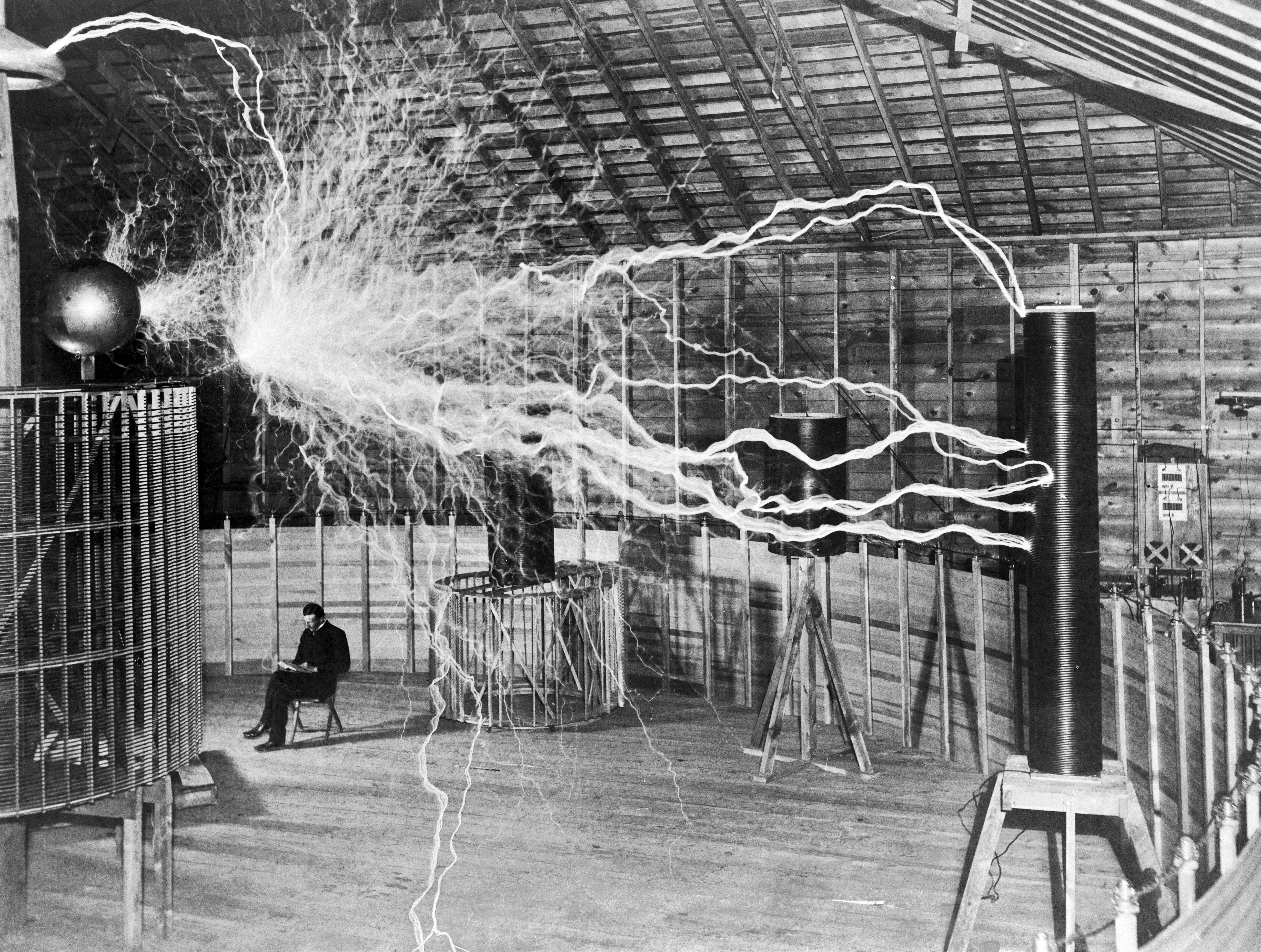 A multiple exposure picture of Tesla sitting next to his "magnifying transmitter" generating millions of volts. The 7-metre (23 ft) long arcs were not part of the normal operation, but only produced for effect by rapidly cycling the power switch.