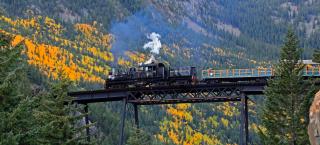 The Georgetown Loop train crosses a bridge. Fall is changing the aspens yellow and green in the background. 