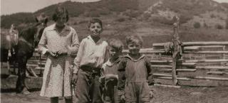 A black and white photograph of four children posing in front of a farm fence on the Redmond Ranch.