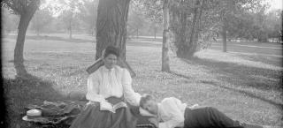Historic photo of woman reading under a tree in a park