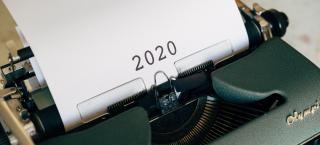 Photo of an old Olympic typewriter, with a piece of white typing paper in it, which simply says "2020" in large black numerals. 
