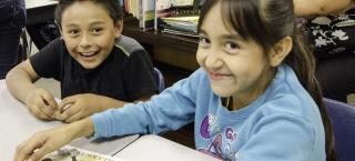 Photo of two elementary students, sitting at a desk together, smiling and playing a game based on the history of Silverton, Colorado.