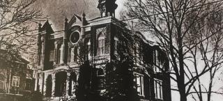 Photo of Temple Aaron, long before the completion of a preservation project. This historic black and white photo shows the brick building sitting on a hill, the slope of the hill visible in the image. There is a front porch made of brick, and a large round window in the building directly above the door. There are gothic style arched windows and decorative finials along the roof of the building.