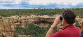 A man looks at ruins with binoculars at Mesa Verde National Park