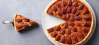 Photo image of a large pecan pie, with pecans spaced beautifully around the top in a circular pattern.  One slice has been cut, and has been lifted out of the pie. The slice is just to the left of the pie, and sits on a pie server.