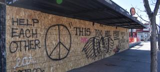 Photo of Think Tank Tattoo, with windows boarded up due to closure during the 2020 pandemic. The main image spray painted on the boards is an eagle and "THIS TOO WILL PASS". Right side detail consists of black outline of a flower, heart and the words, "UNITED WE STAND" and "WE LOVE YOU DENVER!!" 