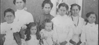 An historic photo of two women sitting amongst one boy and five girls, all ranging in ages from about one year old to teens.