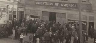 Photo of Volunteers of America office in Denver. Dozens of men dressed in coats and hats stand on the sidewalk outside of the offices. 