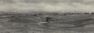 Photo of the Lakewood Country Club in 1921, taken in panoramic view. The golf course is lined with trees on the far side of the photo, and otherwise surrounded by vast open space. The snow-capped peaks of the Front Range are available on the far horizon.