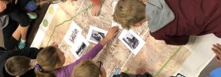 Students using the Ute STEM map on the floor. They are gathered around a map and comparing it to photos.