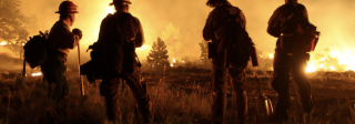 Silhouette of 4 firefighters from the back as they watch a blazing wildfire.