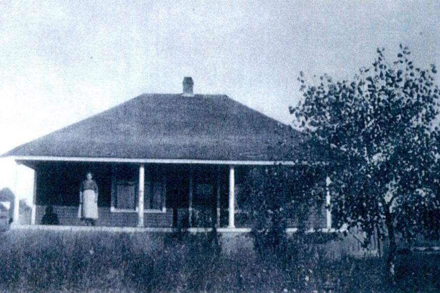 Mrs. Kochis stands on the front porch of original homestead, 1919.