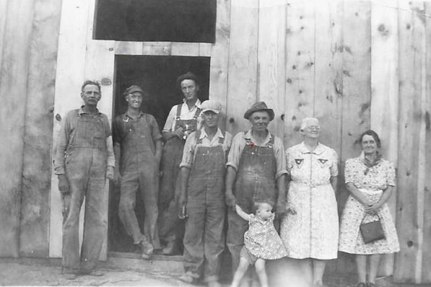 Several generations of the Coe Homestead stand in front of a barn door in this historic photograph.