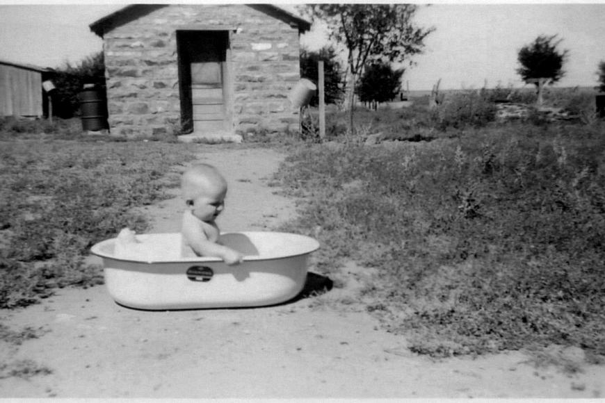 Toddler Connie Fulbright in a wash tub outside the wash house on the farm, 1949.