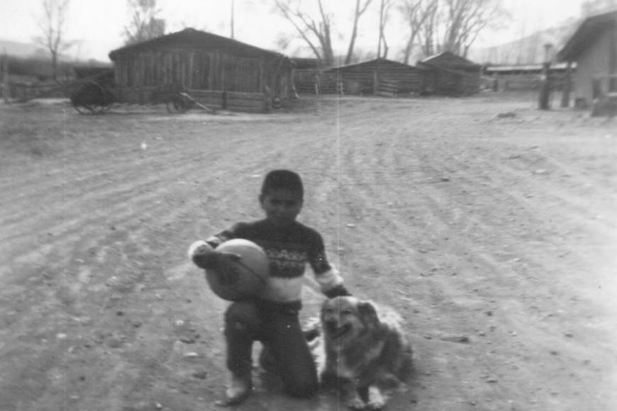 A boy and dog in a 1960 photo of the Knoblauch Ranch.  The horse barn, granary and milk cow barn are in the background.