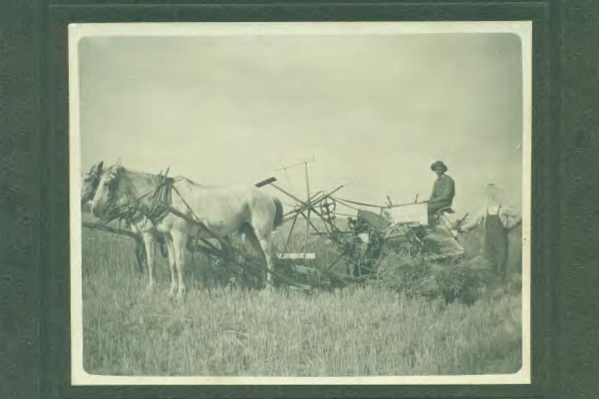 Historic photo showing two men standing next to, and on, farm equipment.