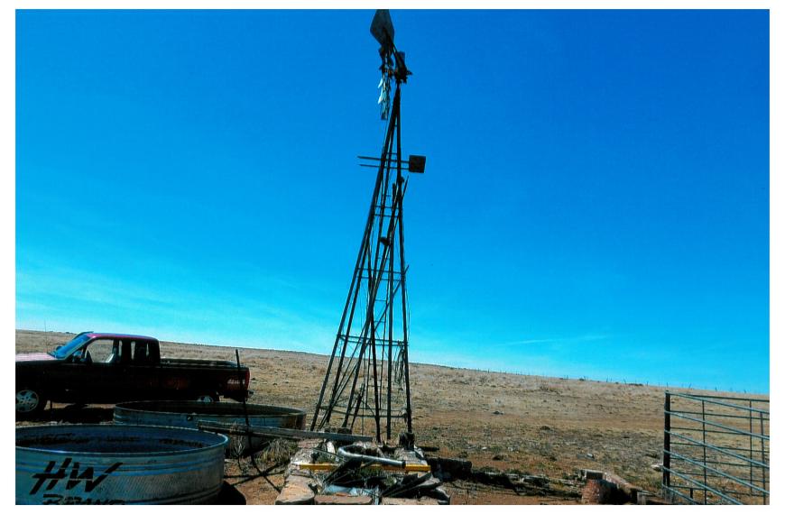 A metal windmill standing on the old rock tank on the Darnell Ranch, set against a striking blue sky.
