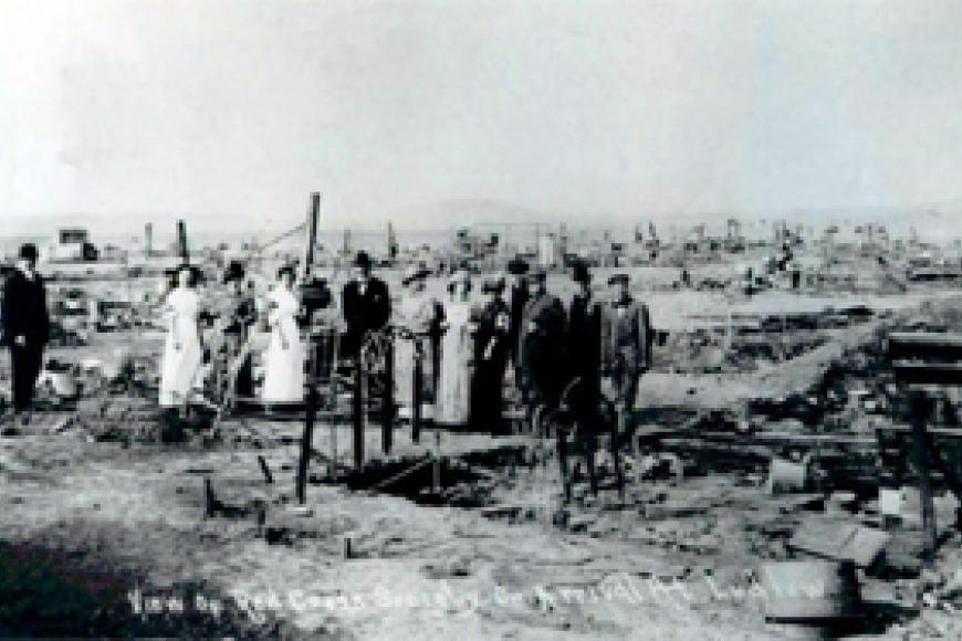 A black and white photo of the site around the time of the event with a group of people standing in the center of the pictures.