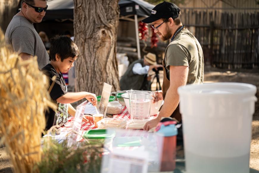 A group of people at a booth at the El Pueblo History Museum Mercado (market) at the Pueblo Chile Fest. They are examining historic and traditional varieties of wheat and other grains.