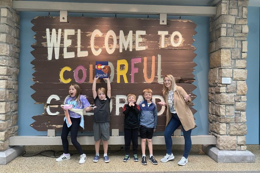 Fourth grade students, all members of the History Buffs membership program for students, pose with their History Buffs packets in front of the Welcome to Colorful Colorado sign at the History Colorado Center.