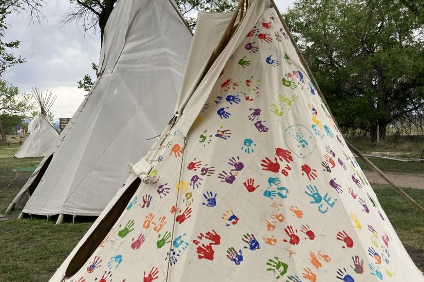 A tipi at the Ute Indian Museum, made of white fabric. The fabric is covered in multicolored handprints, which were added by museum members at a community event.