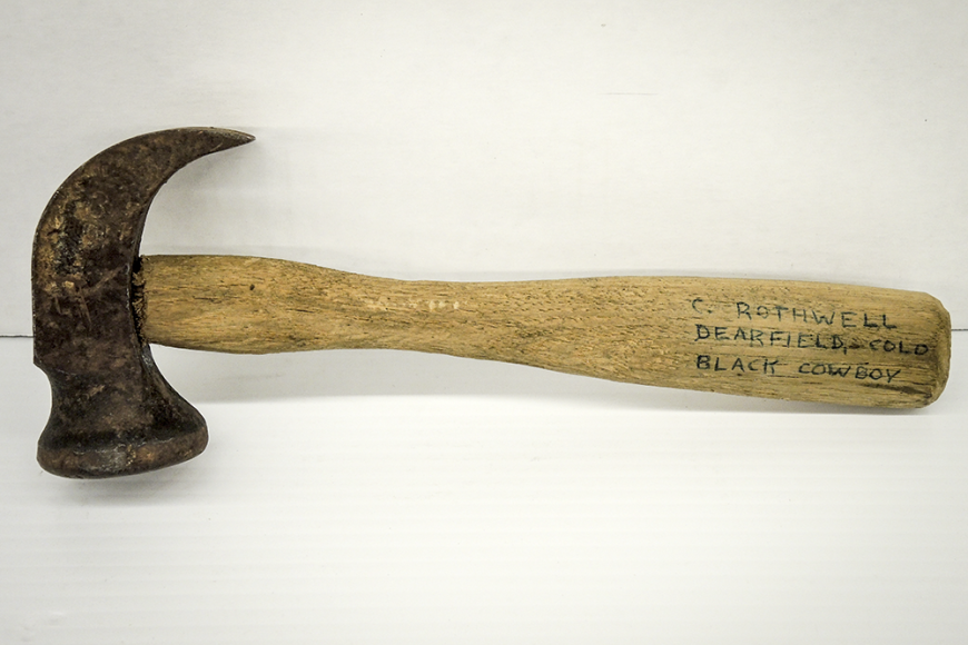 A claw-hook hammer of old fashioned design, with a worn wooden handle and a sturdy metal head.