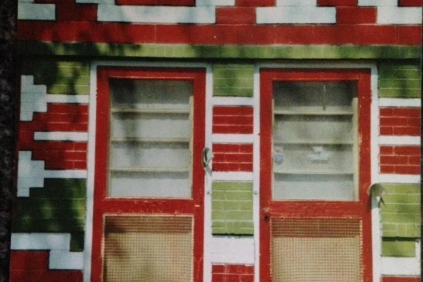 A colorful geometric mural in red, white, and green adorns the front of a residential building with two doors.