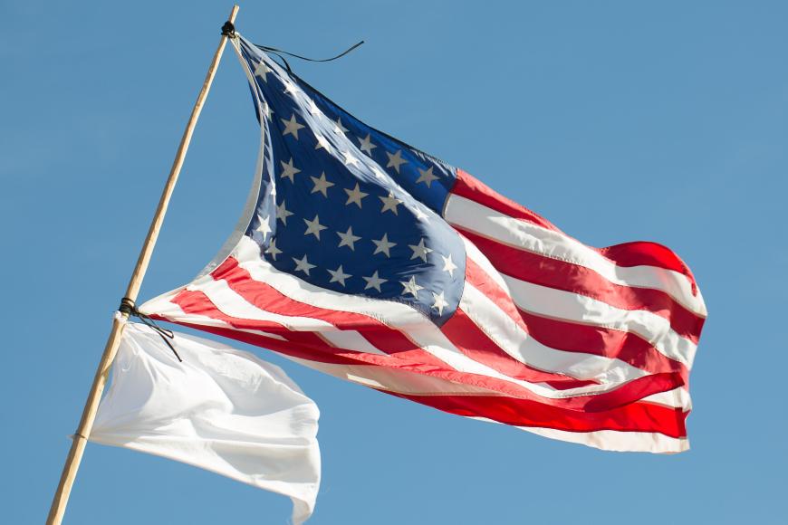 Two flags flying- one the flag of the United States, the other a white flag of peace.