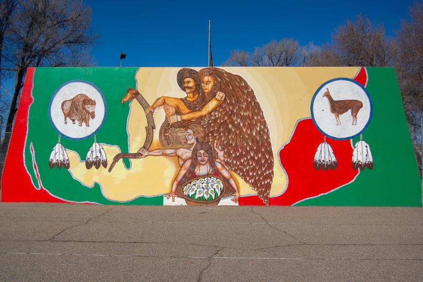 A mural in red, gold, and green, evoking the flag of Mexico and depicting two individuals, a man and a woman, standing in Central America with North America to their left and South America to their right.