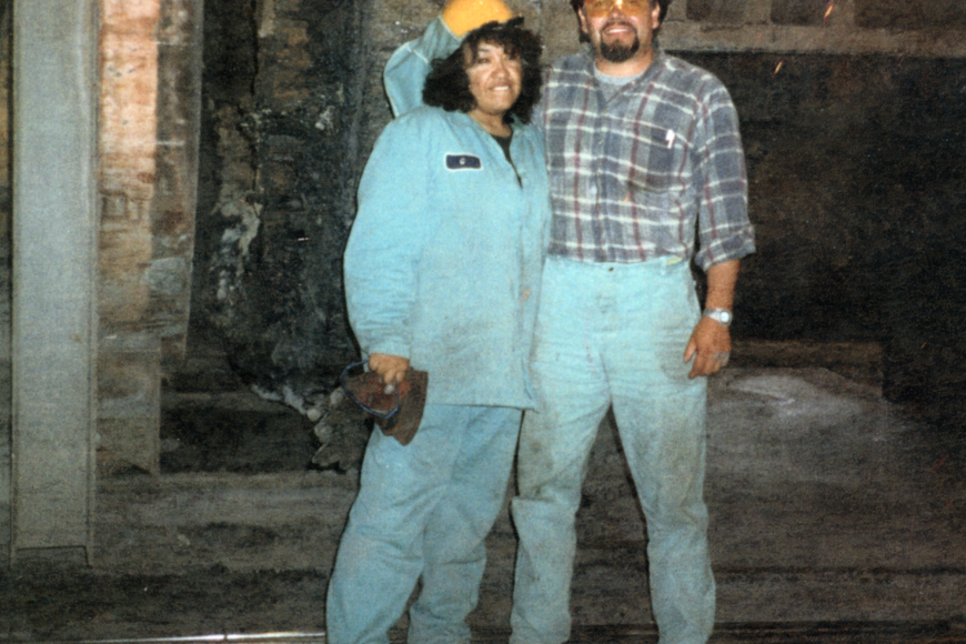 A male and female steel worker wearing coveralls and hard hats in the steel mill, 1980s.
