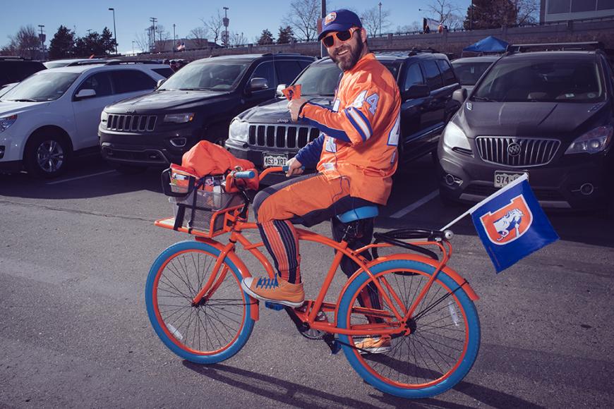 Broncos superfan in a Broncos jersey, riding a blue and orange bike.