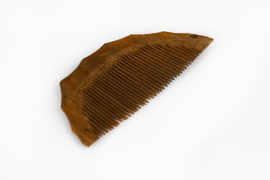 A thin carved wooden comb. It is made from dark wood and in a semi-circle shape.