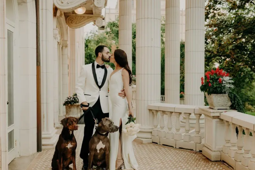 A newlywed couple on the porch of Grant Humphreys Mansion with their two dogs. They are kissing.