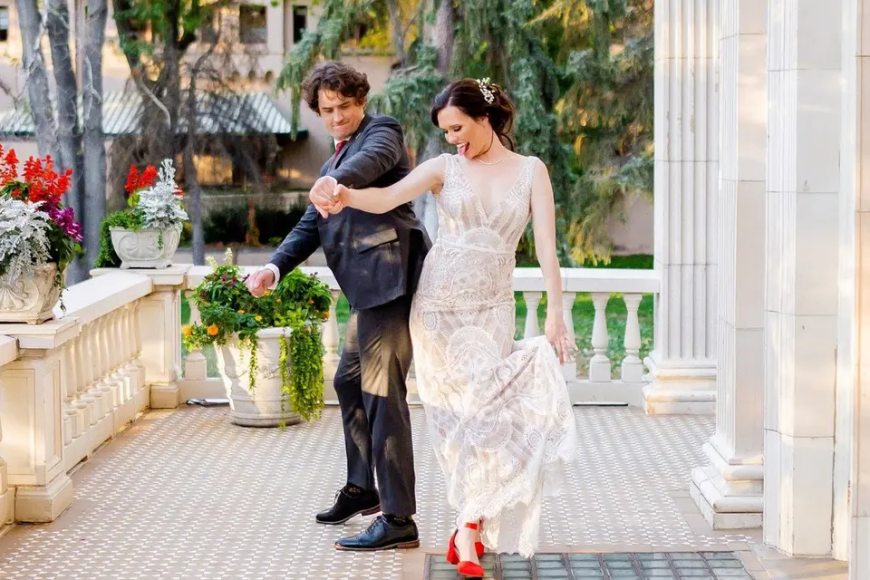 A bride and groom dancing gracefully outside the entrance of Grant Humphreys Mansion. She is wearing a notable pair of red heels while she twists.