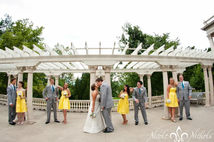A bridal part in grey and yellow suits and dresses. They pose happily on the terrace of Grant Humphreys Mansion while the Bride and Groom kiss.