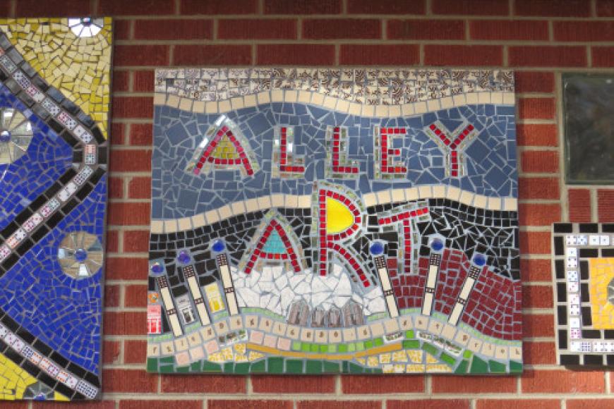Bonnie Brae Art alley mosaic on a brick wall. The text reads alley art made from blue and red stone.