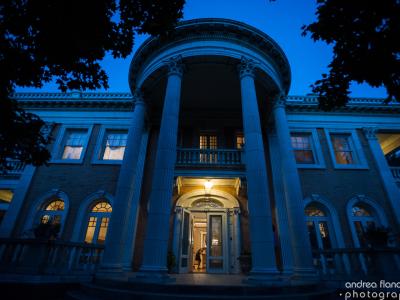 A photograph of the front facade of the Grant-Humphreys Mansion at night. The house is mostly shrouded in blue near-darkness, but lights are on inside.