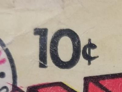 Photo of a fragment from the cover of a comic book. While the title of the comic book is missing, the price of 10 cents is clearly visible, printed in black ink on white paper. A fraction of red ink is directly below the printed price, although its lettering or image is unidentifiable. 
