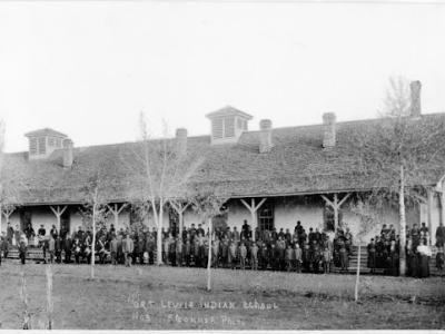 Photo of a long, one-story building that is part of the Fort Lewis Indian School. Students from the school are lined up in rows along the building front in this historic photo.  Handwriting at the bottom of the photo says "Fort Lewis Indian School No. 3 F. Gonner Photo."