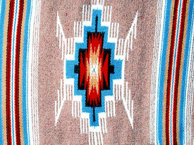 Photo of a woven piece by Eppie Archuleta called "Rain Cloud." The piece features a tan background, with horizontal thin stripes clustered together into two wide horizontal bands on each side of the image. These stripes are white, turquoise, red, and black in color. The center image is a blocky geometric shape of turquoise, black, red, and tan, with white feather-like edging. There is a very small turquoise dot in the very center.