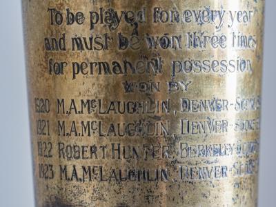 Photo closeup of the inscription on a silver-plated vase that shows some tarnish. The trophy pictured is the original presented to the winner of the Pebble Beach Golf Tournament, which began in 1920. The inscription shows that M.A.McLaughlin won the trophy in 1920, 1921, and 1923. A Robert Hunter won it in 1922.
