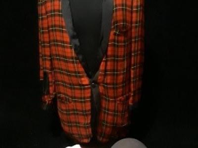 Photo of the outfit worn by TV personality Blinky the Clown. The red plaid jacket has a black satin narrow rounded lapel, and the jacket is hung on a mannequin for display. Blinky's gray bowler hat is displayed in front of the jacket, as are Blinky's white gloves.