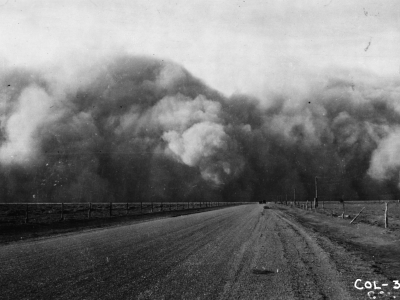 A black and white photo depicts a cloud of dust over a barren field. 