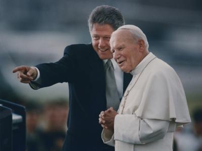 President Bill Clinton and Pope John Paul II stand before a crowd, smiling.