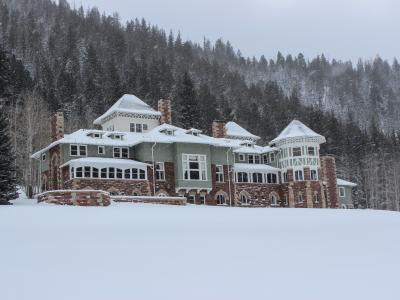 A turn of the century manor with a broad, snow-covered lawn and a dense forest behind it.