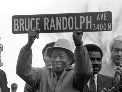Bruce Randolph holding up a street sign which reads: "Bruce Randolph, Ave."